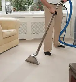 Professional carpet cleaner using a hot-water extraction wand and hose machine in a living room in Hollywood, FL.