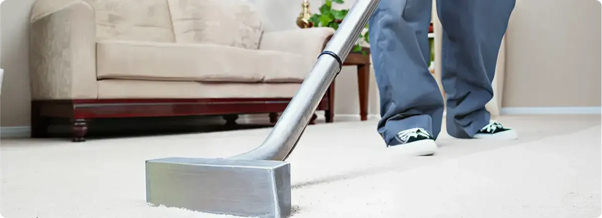 Carpet cleaning technician using a hot-water extraction wand on a light-colored carpet in a living room, Hollywood, FL.