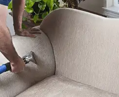 Professional upholstery cleaner deep-cleaning a fabric sofa with a handheld extraction tool and hose in Hollywood, FL.